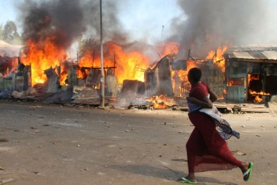 A pregnant woman runs past burning shacks in Nairobi's Mathare slum during 2007 post-election violence (file photo).