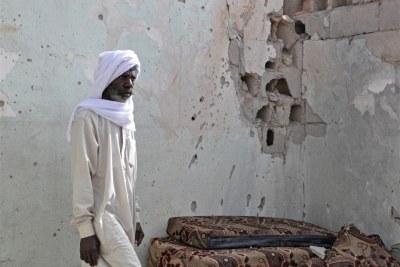 A resident of Tayuri stands against a bullet-riddled wall of his house.
