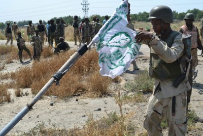 A Nigerian soldier pull down a Boko Haram flag as a mark of victory (file photo).